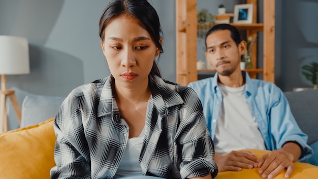 Verärgertes asiatisches Paar sitzt auf der Couch im Wohnzimmer