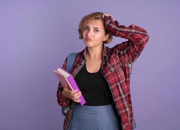 Verärgertes junges slawisches Studentenmädchen, das Rucksack trägt, legt Hand auf Kopf hält Buch und Notizbuch