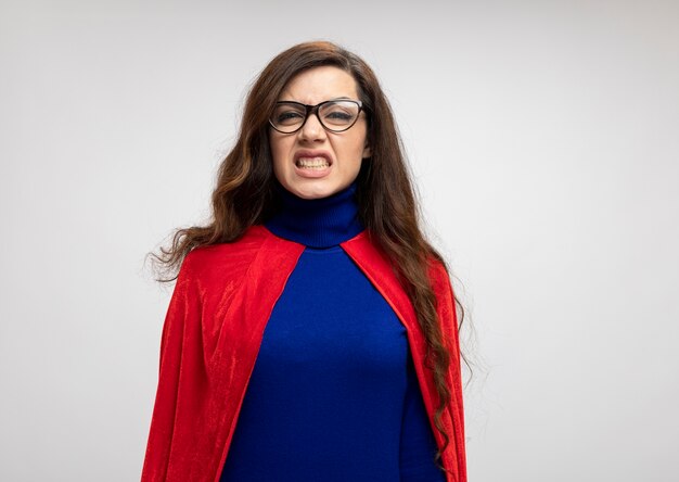 Verärgertes kaukasisches Superheldenmädchen mit rotem Umhang in optischer Brille betrachtet Kamera auf Weiß