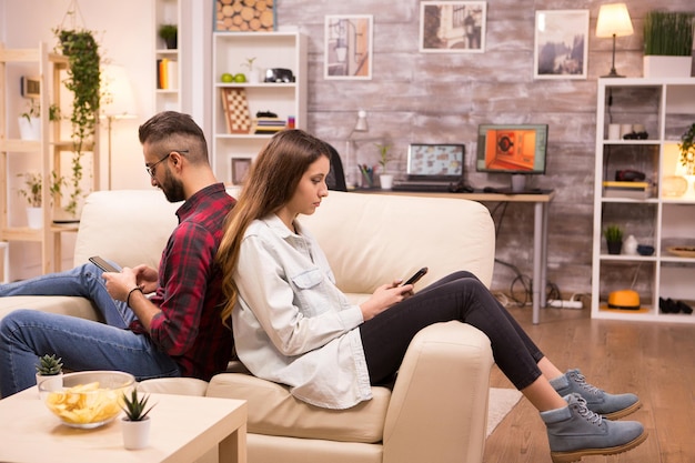 Verärgertes Paar, das nach einer Meinungsverschiedenheit Rücken an Rücken auf dem Sofa im Wohnzimmer sitzt.