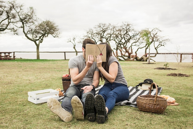 Verbinden Sie das Sitzen auf der Decke, die Buch über ihrem Gesicht am Picknick hält