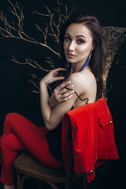 Verführerische Frau im roten Anzug sitzt vor einem glänzenden Baum