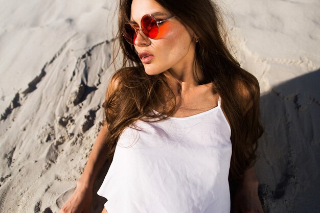 Verführerische junge Frau in roten Sonnenbrillen liegt auf weißem Sand