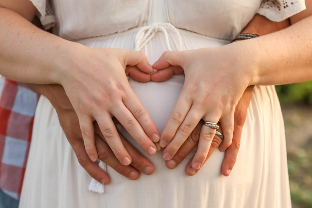 Verheiratetes Paar, das eine Herzform mit den Händen auf dem schwangeren Bauch der Frau bildet