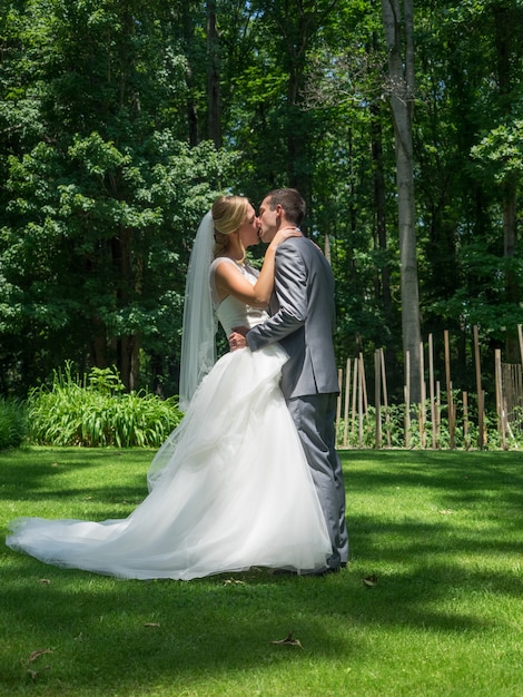 Verheiratetes Paar, das in einem Garten küsst, der durch Grün unter Sonnenlicht umgeben ist
