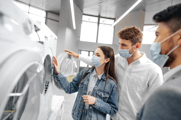 Verkäufer im SB-Warenhaus mit medizinischer Maske zeigt seinen Kunden eine neue Waschmaschine