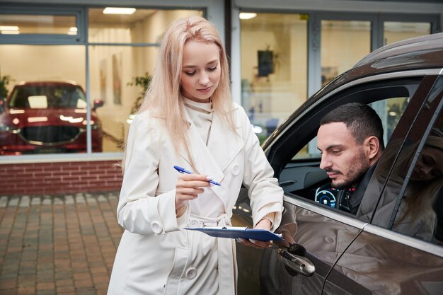 Verkäuferin, die darum bittet, einige Dokumente im Autohaus zu unterschreiben