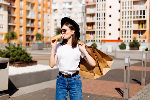 Verkaufs-, Konsum-, Sommer- und Personenkonzept. Glückliche junge Frau mit Einkaufstüten und Eis auf Stadtstraße