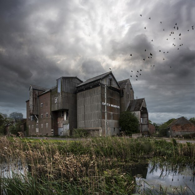 Verlassene Mühle mit einem dunklen Himmel und Vögeln, die in North Norfolk, Großbritannien fliegen