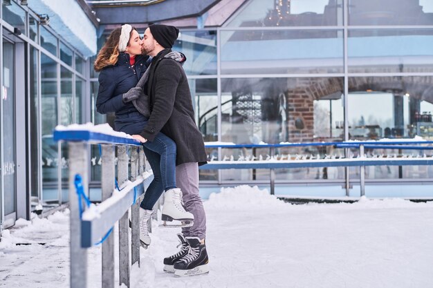 Verliebtes Paar, Date auf der Eisbahn, ein Mädchen, das auf einer Leitplanke sitzt und sich mit ihrem Freund umarmt.