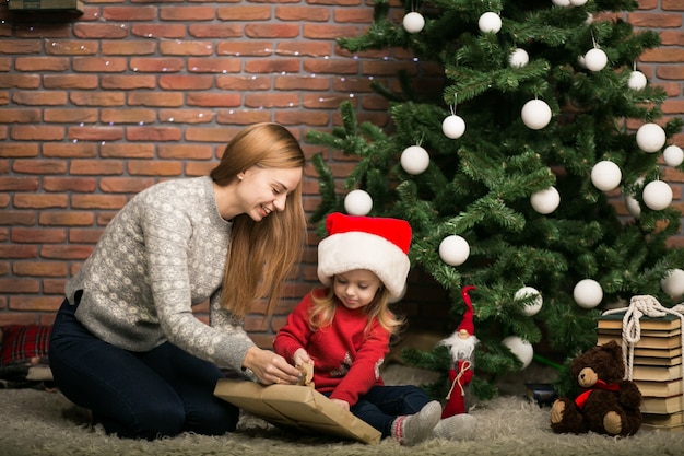 Verpackengeschenke der Mutter und der Tochter durch den Weihnachtsbaum