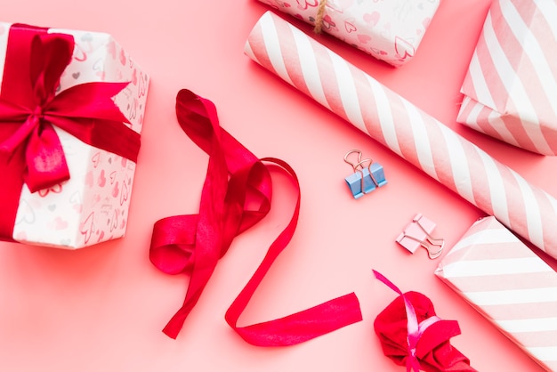 Verpackte Geschenkbox mit rotem Band; Geschenkpapier und Büroklammer auf rosa Hintergrund