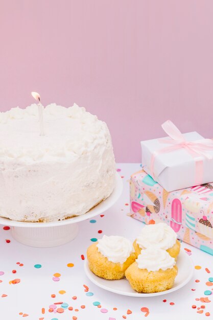 Verpackte Geschenke; Cupcake und Kuchen mit Kerze am Geburtstag vor rosa Hintergrund