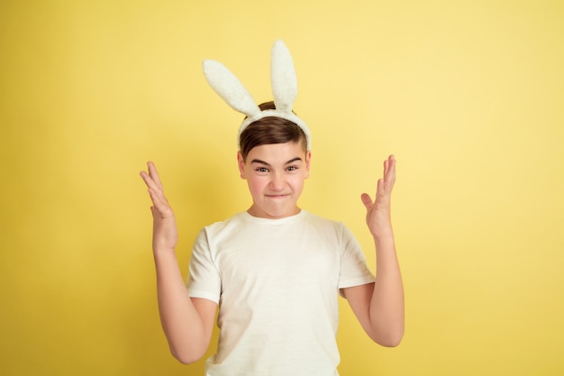 Verrückt nach oben zeigen. Kaukasischer Junge als Osterhase auf gelbem Studiohintergrund. Fröhliche Ostergrüße. Schönes männliches Modell. Konzept der menschlichen Gefühle, Gesichtsausdruck, Feiertage. Copyspace.