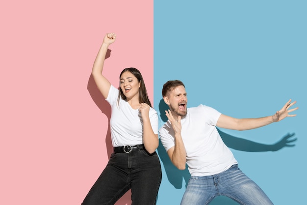 Verrückt. Tanzen, Bewegen, Spaß haben. Junger und glücklicher Mann und Frau in Freizeitkleidung an rosa, blauer zweifarbiger Wand. Konzept der menschlichen Emotionen, Gesichtsausdruck, Beziehungen, Anzeige. Schönes Paar.