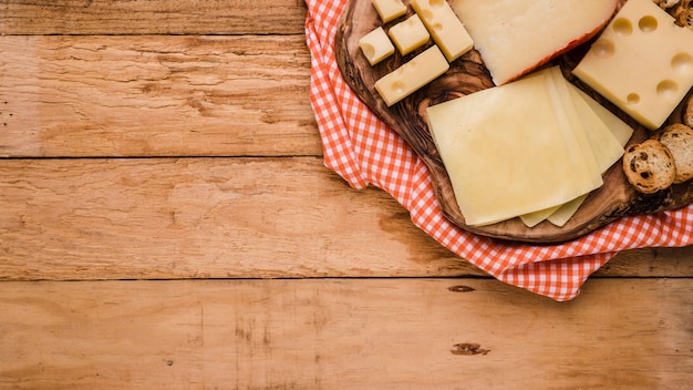 Verschiedene Arten von Käse auf hölzernem Untersetzer mit Tischdecke über Bank