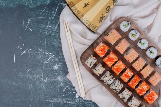 Verschiedene Arten von Sushi-Rollen auf Holzplatte mit Stäbchen und japanischem Fächer serviert.