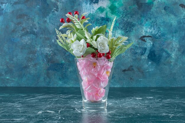 Verschiedene Blumen in einem Glas, auf blauem Hintergrund.