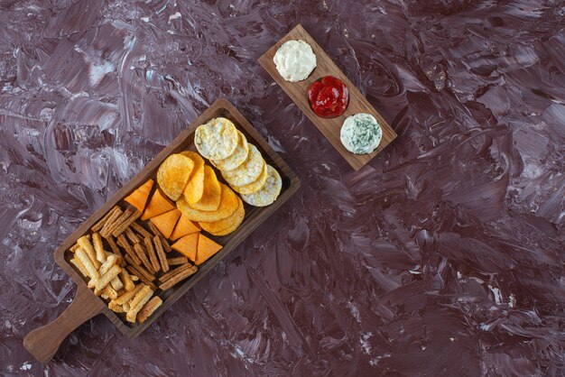 Verschiedene Chips auf Servierbrett mit Soße, auf dem Marmortisch.