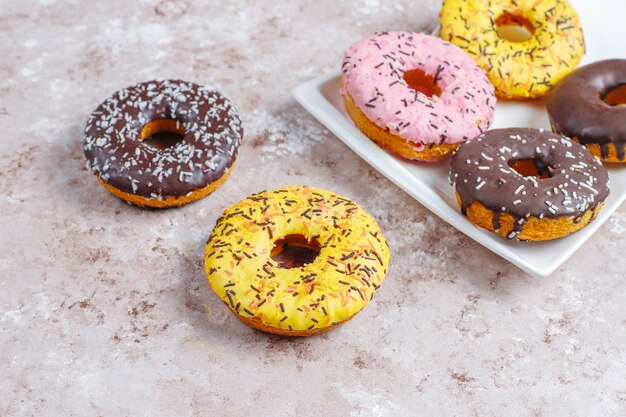 Verschiedene donuts mit schokoladenglasur, rosa glasiert und streuseln.