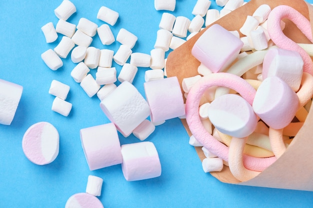 Verschiedene formen von marshmallows in papier eingewickelt auf blauem hintergrund, nahaufnahme, umweltfreundliche süßigkeitenverpackung, süße perkussion