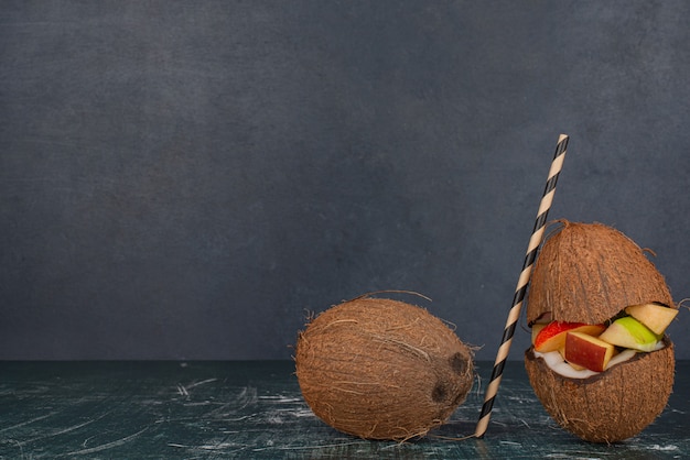 Verschiedene Früchte in halb geschnittener Kokosnuss mit Stroh auf Marmortisch
