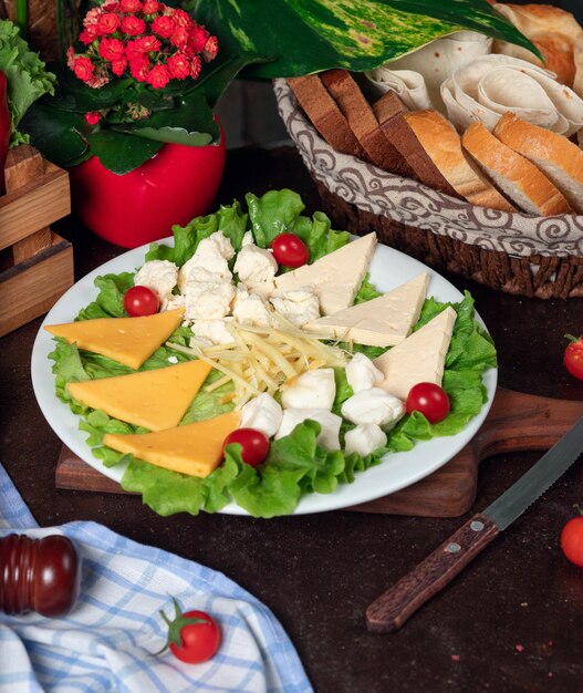 Verschiedene Käsesorten befinden sich auf einem Holzbrett und sind mit Kirschtomaten, Salat und frischem Brot dekoriert.