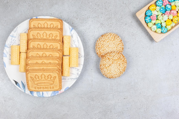 Verschiedene Kekse auf einem Teller mit zwei Keksen neben Bonbons auf Marmorhintergrund. Hochwertiges Foto