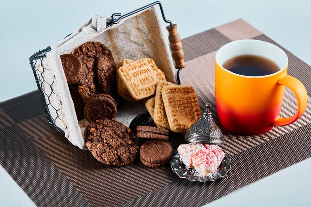 Verschiedene Kekse, Süßigkeiten und eine Tasse Tee auf grauer Oberfläche.