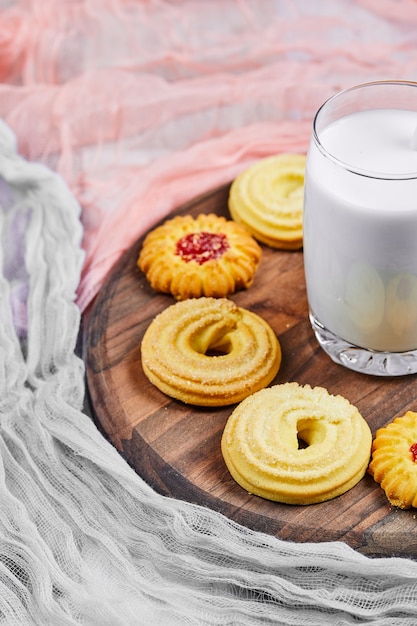 Verschiedene Kekse und ein Glas Milch auf einem Holzteller.