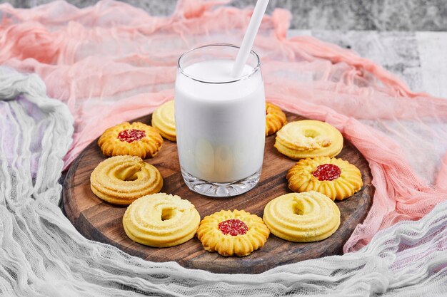 Verschiedene Kekse und ein Glas Milch auf Holzteller mit Tischdecken.