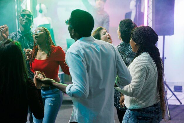 Verschiedene Menschen feiern und tanzen gemeinsam bei einer Diskothekenparty im Nachtclub. Junge Freunde halten Händchen, singen und entspannen sich auf der überfüllten Tanzfläche bei geselligem Beisammensein