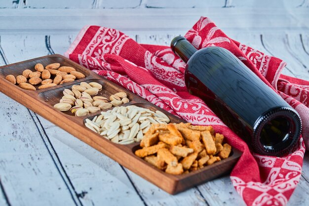 Verschiedene Snacks und eine Flasche Wein auf dem blauen Tisch. Cracker, Sonnenblumenkerne, Pistazien, Mandeln.