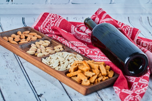 Verschiedene Snacks und eine Flasche Wein auf dem blauen Tisch. Cracker, Sonnenblumenkerne, Pistazien, Mandeln.