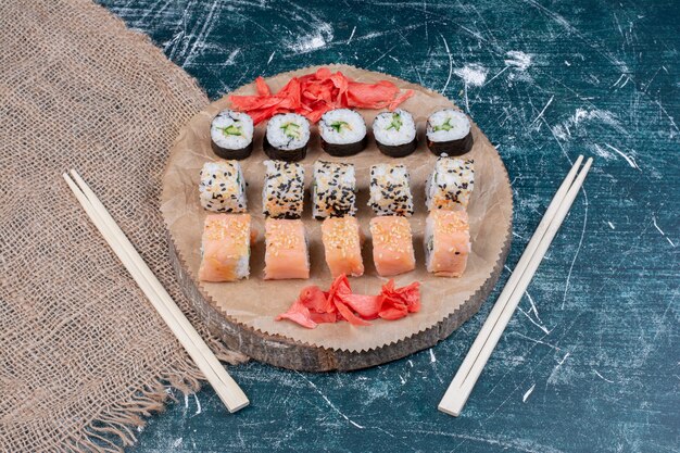 Verschiedene Sushi-Rollen auf Holzplatte mit eingelegtem Ingwer und Essstäbchen.