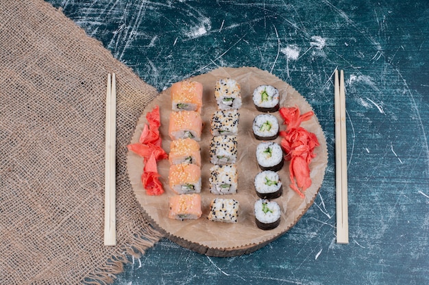 Verschiedene Sushi-Rollen auf Holzplatte mit eingelegtem Ingwer und Essstäbchen.