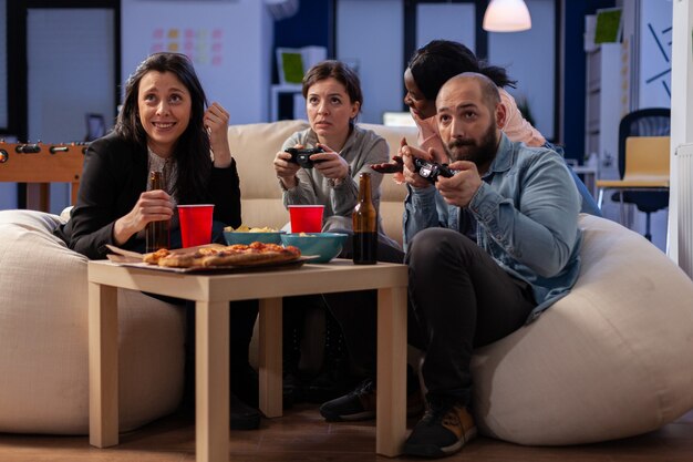 Verschiedenes Team von Mitarbeitern, die nach der Arbeit im Büro Konsolenspiele im Fernsehen mit Joysticks spielen