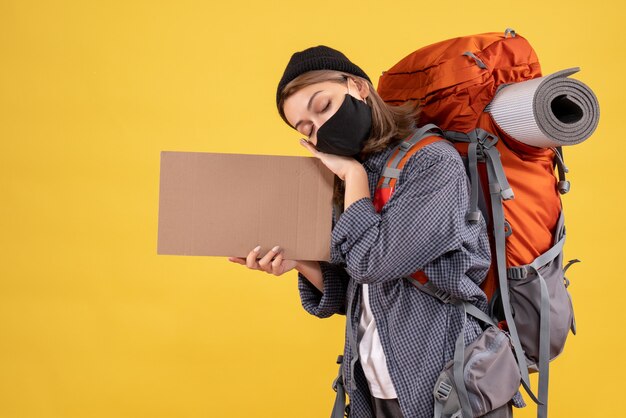 verschlafene Reisende mit schwarzer Maske und Rucksack mit Karton