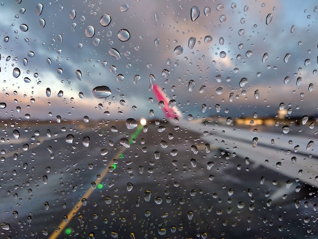 Verschwommene Ansicht einer Landebahn des Flughafens durch ein Flugzeugfenster mit Regentropfen