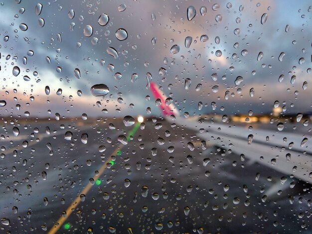 Verschwommene Ansicht einer Landebahn des Flughafens durch ein Flugzeugfenster mit Regentropfen