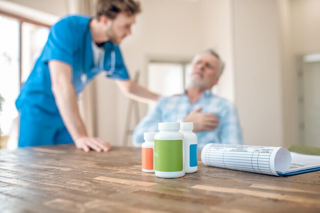 Verschwommenes Foto eines dunkelhaarigen bärtigen Kardiologen in Uniform, der sich über einen grauhaarigen kaukasischen Patienten mit Herzinfarkt beugt