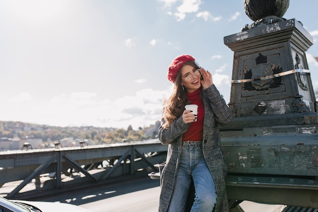 Kostenloses Foto verspielte kaukasische frau in den jeans, die kaffee trinken, während sie europäische stadt erkunden