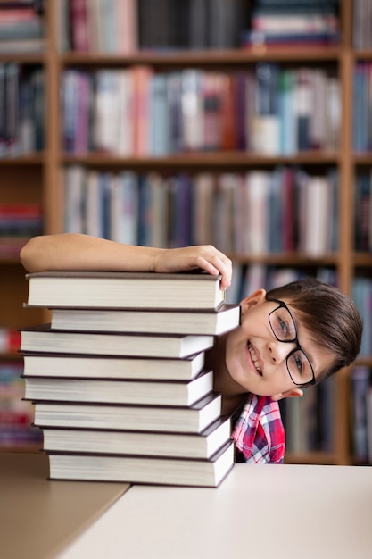 Kostenloses Foto verspielter junge, der sich hinter einem stapel bücher versteckt