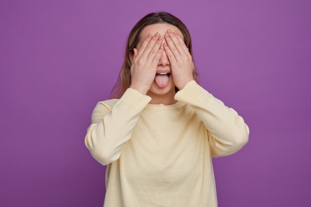 Verspieltes junges Mädchen, das Augen mit Händen bedeckt, die Zunge zeigen