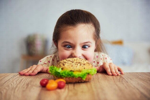 Verspieltes Mädchen, das köstlichen Hamburger betrachtet