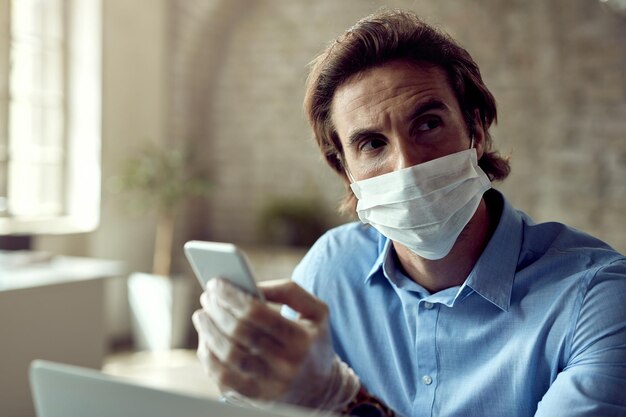 Verstörter Geschäftsmann benutzt Handy und denkt während der Arbeit im Büro während der Coronavirus-Epidemie nach