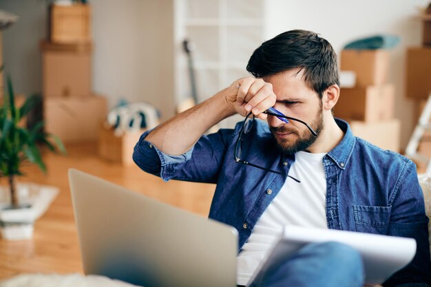 Verstörter Mann, der eine E-Mail auf dem Laptop liest, während er in ein neues Zuhause zieht