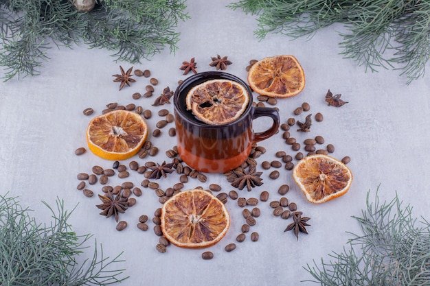 Verstreute Anissamen, getrocknete Orangenscheiben und eine Tasse Tee auf weißem Hintergrund.