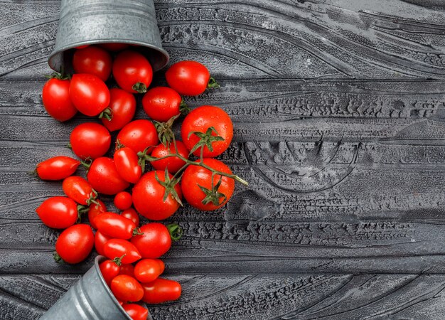 Verstreute Tomaten aus Mini-Eimern auf einer grauen Holzwand. Draufsicht.