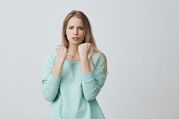 Verteidigung und Schutz. Starke Sportfrau, die Freizeitkleidung mit blonden Haaren und ernstem, selbstbewusstem Blick trägt und die Fäuste vor sich geballt hält, um sich vor Beleidigungen und schlechter Behandlung zu schützen